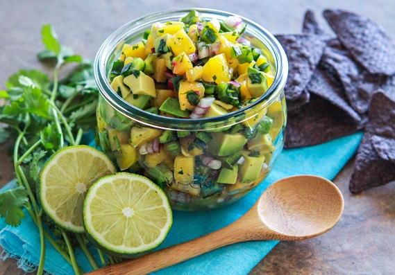photo of Avocado Peach Salsa in a jar with a serving spoon and blue corn tortilla chips
