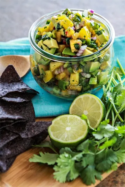 photo of Avocado Peach Salsa in a jar with fresh limes and cilantro leaves