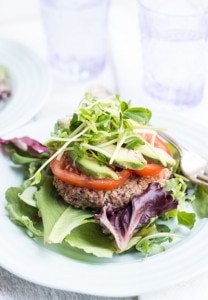 Black Bean Quinoa Burger patty on lettuce with sliced tomato and greens on top