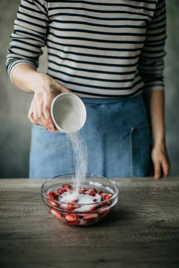 woman pouring sugar on a bowl of strawberries