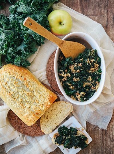 Overhead view of braised kale in a white serving dish next to a loaf of bread.