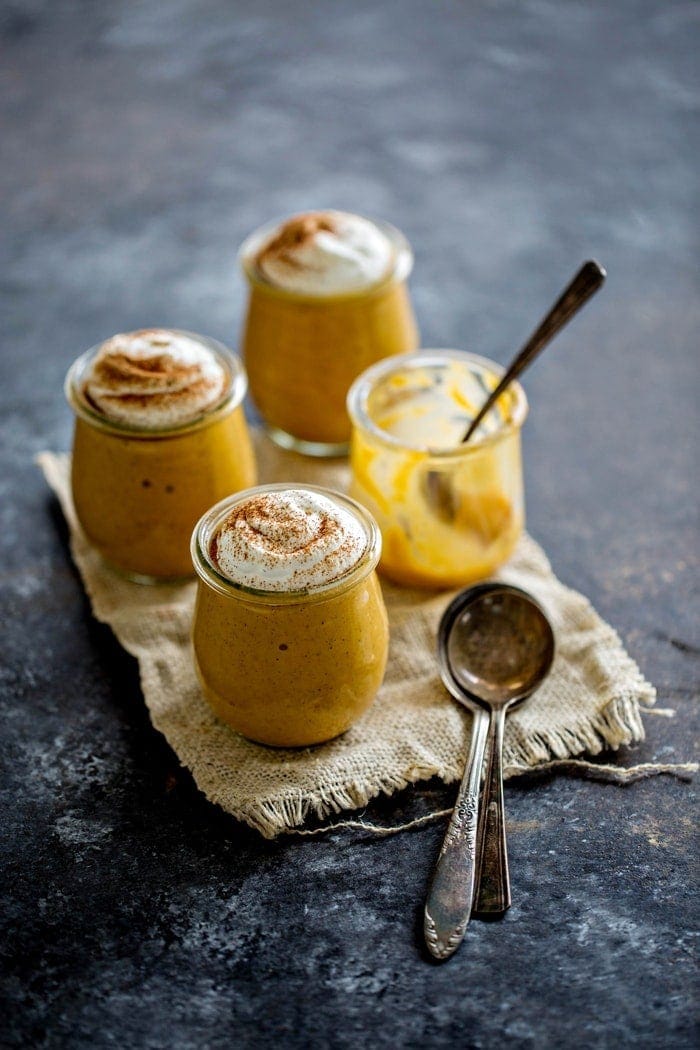 Four jars, three of which are filled with pumpkin spice pudding and garnished with whipped cream. The fourth jar has been eaten. 