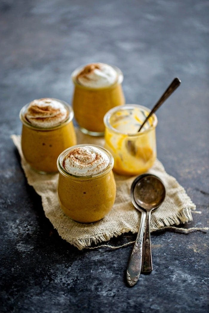 Four jars, three of which are filled with pumpkin spice pudding and garnished with whipped cream. The fourth jar has been eaten.