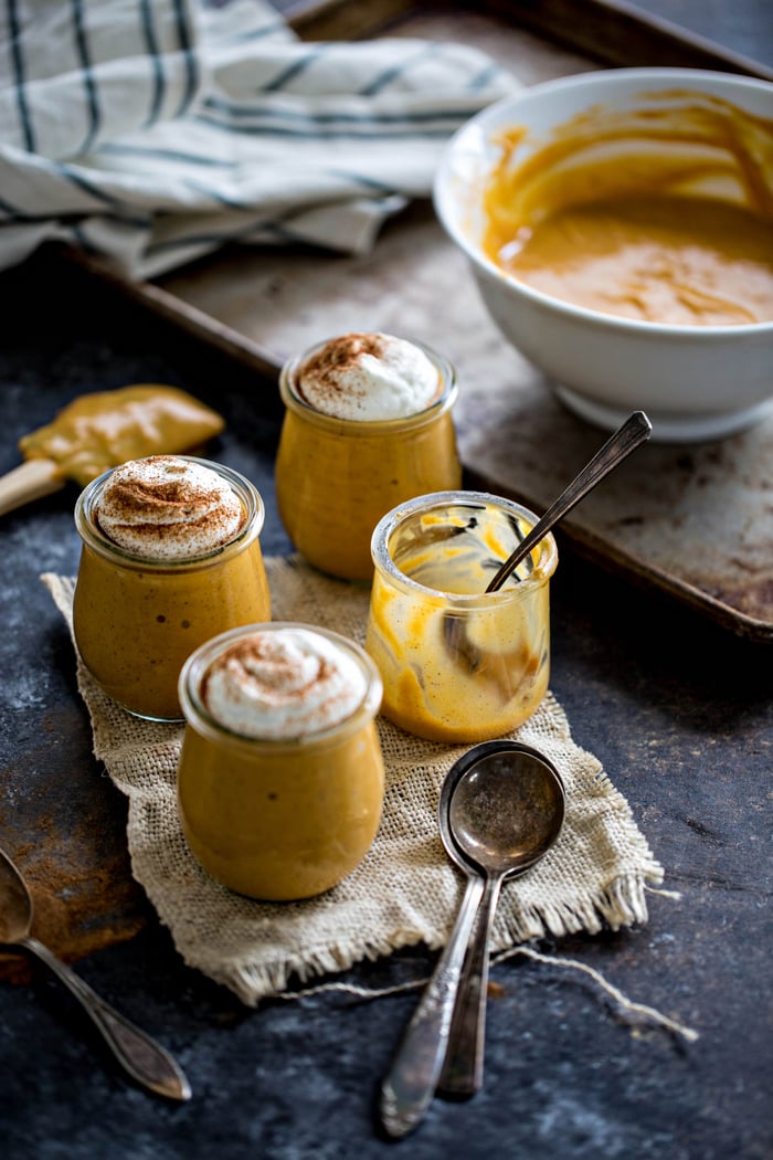 Four jars of pumpkin pudding, with one jar empty. A bowl of pudding rests in the background. 
