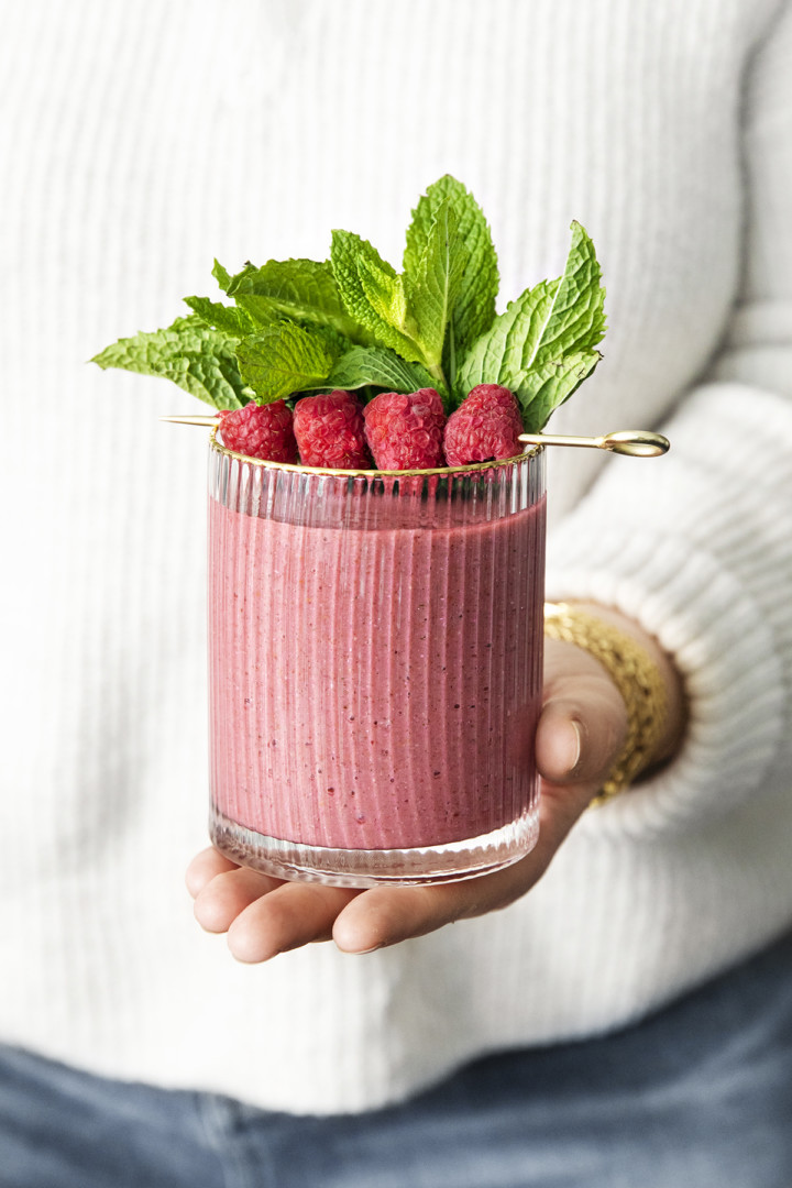 woman holding a glass of minty raspberry banana smoothie