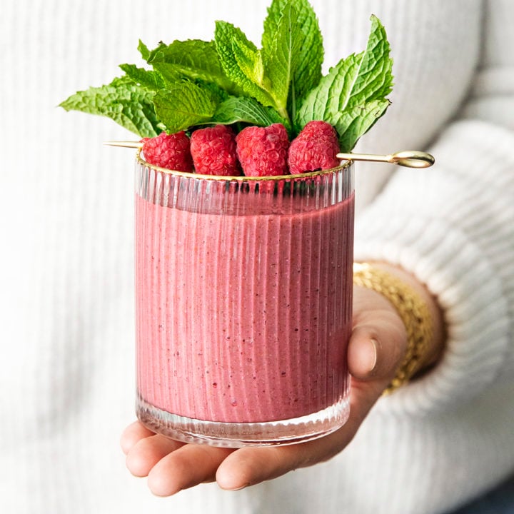 woman holding a glass of minty raspberry banana smoothie