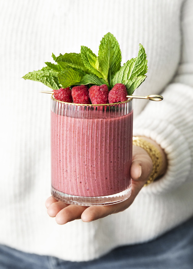 woman holding a glass of minty raspberry banana smoothie