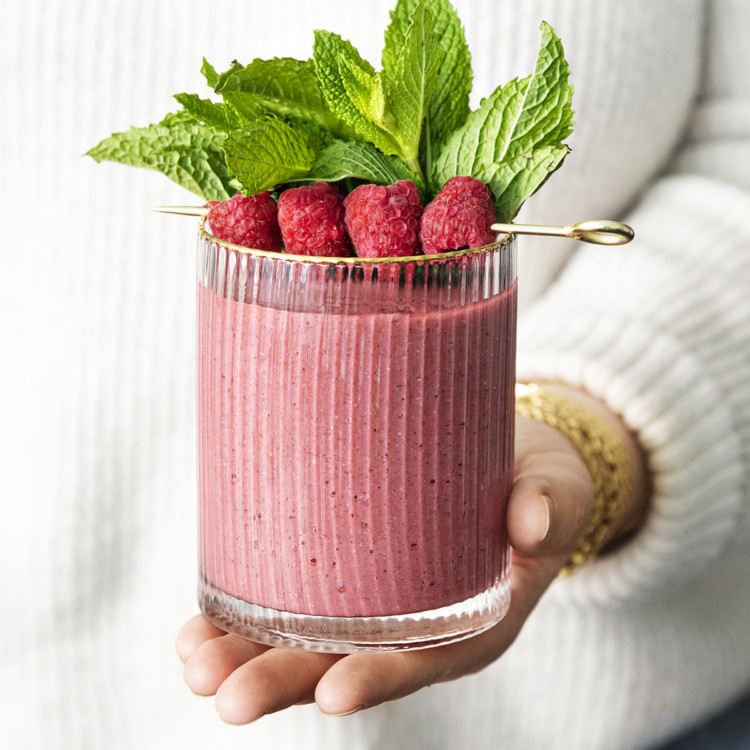 woman holding a glass of minty raspberry banana smoothie