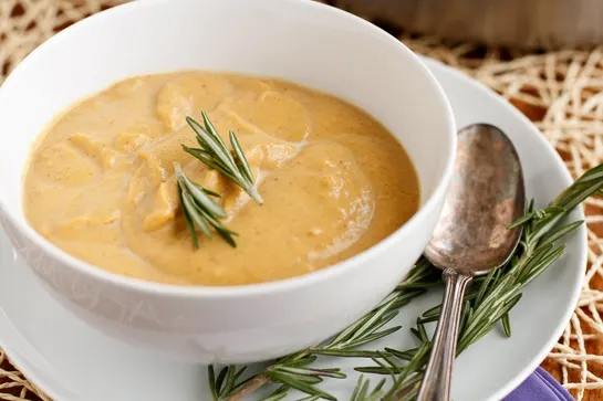 A bowl of creamy butternut squash soup garnished with fresh rosemary.