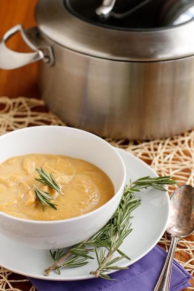 A bowl of creamy butternut squash soup garnished with fresh rosemary.