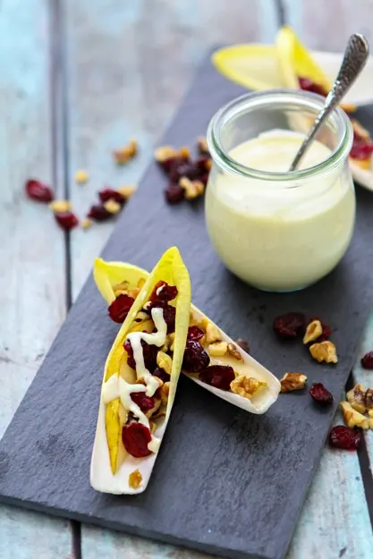 Two Pear, Walnut, and Endive Appetizer Bites with a jar of dressing on a dark tray. 