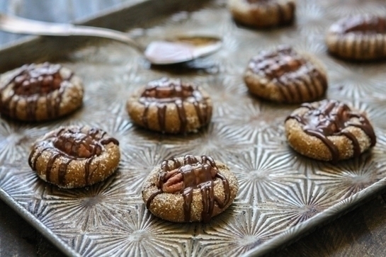 Caramel Pecan Thumbprint cookies on a baking sheet, drizzled with chocolate. 