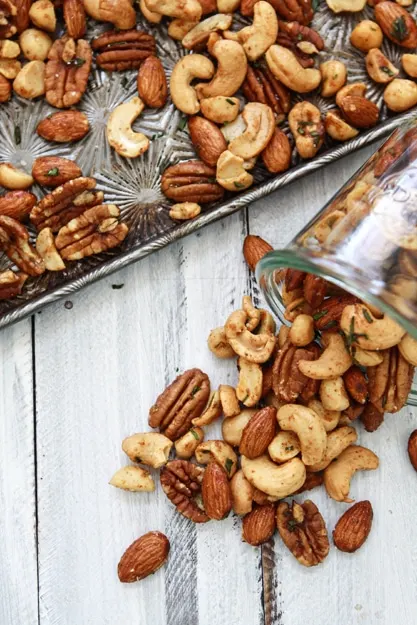 photo of a jar of sweet and spicy rosemary mixed bar nuts next to a baking sheet of roasted bar nuts