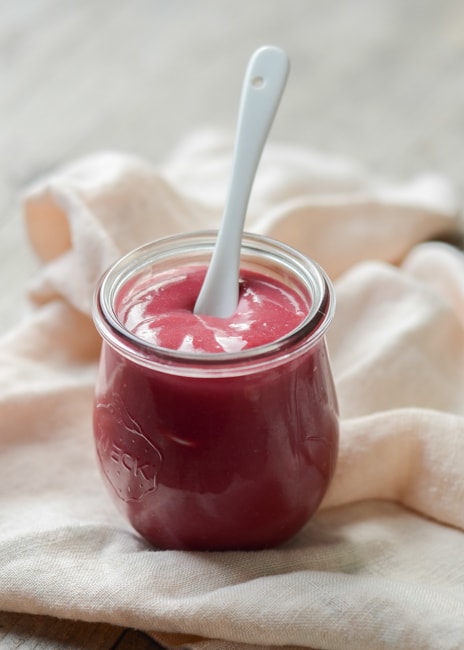 photo of a jar filled with raspberry curd on a table with linens