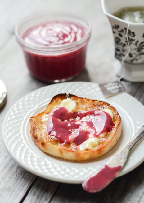 an english muffin on a white plate with butter and raspberry curd