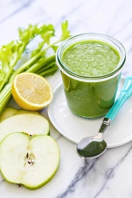 kale pineapple smoothie next to sliced green apple, lemon, and celery