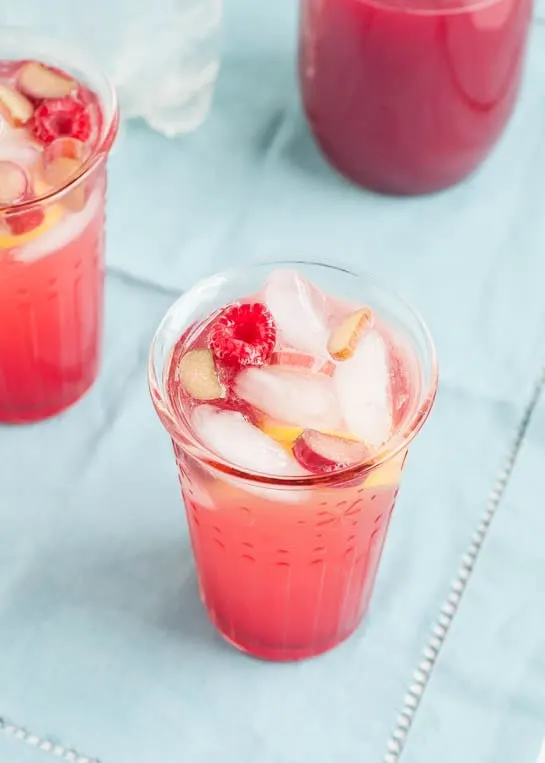 rhubarb lemonade in a glass with raspberries and rhubarb slices on a blue tablecloth