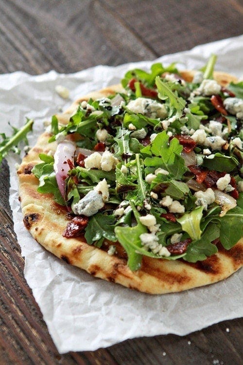 A grilled flatbread pizza topped with bacon, blue cheese, and arugula. 