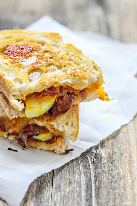 An apple bacon grilled cheese sandwich, cut in half and stacked atop itself. 