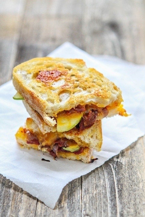 An apple bacon grilled cheese sandwich, cut in half and stacked atop itself. 