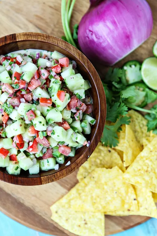 creamy cucumber salsa in wooden bowl next to chips and fresh veggies