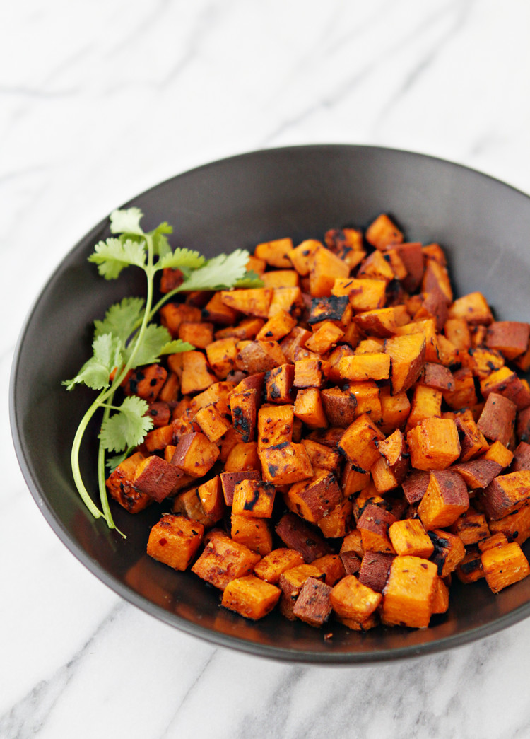 photo of freshly grilled sweet potatoes in foil, golden and caramelized, served in a black bowl with a sprig of cilantro—an easy and delicious summer side dish with smoky southwestern flavors