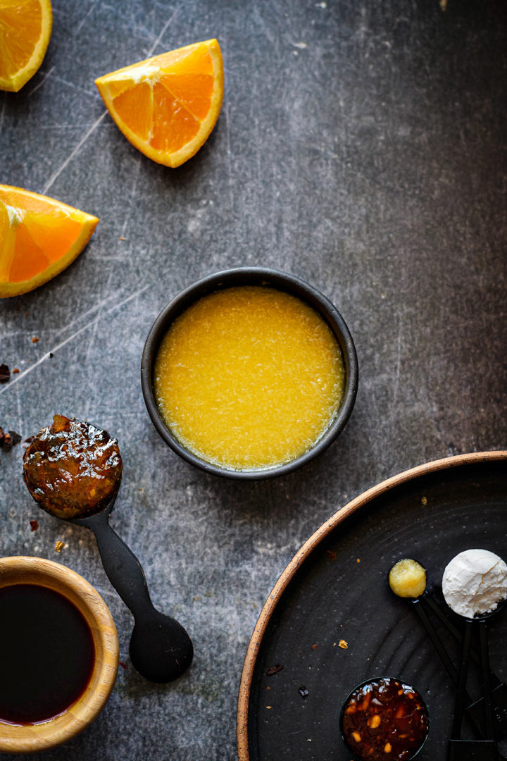 Flat lay of ingredients used to make orange marmalade sauce for chicken. Includes a jar of orange marmalade, soy sauce, garlic, vinegar, and red pepper flakes, all arranged on a neutral background. These simple pantry staples come together to make a flavorful orange chicken sauce with orange marmalade.