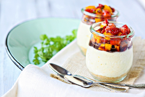 Two no bake mango lime cheesecake cups in glass jars. 