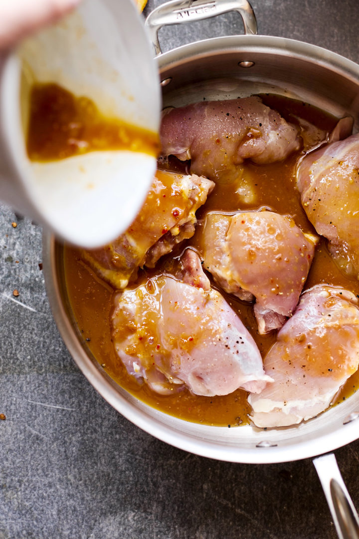 Woman pouring orange marmalade sauce on seasoned chicken thighs in a stainless steel pan