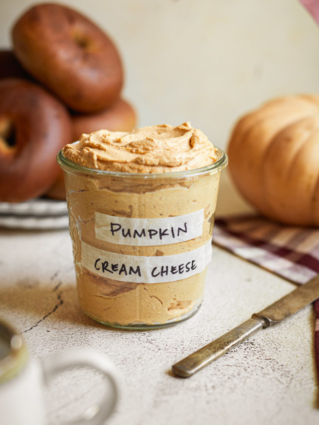 a jar of pumpkin cream cheese spread next to a plate of bagels