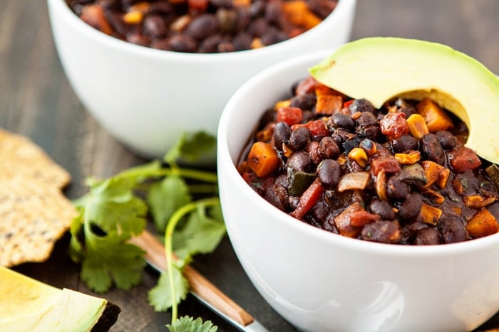 two bowls of butternut squash black bean chili garnished with avocado slices