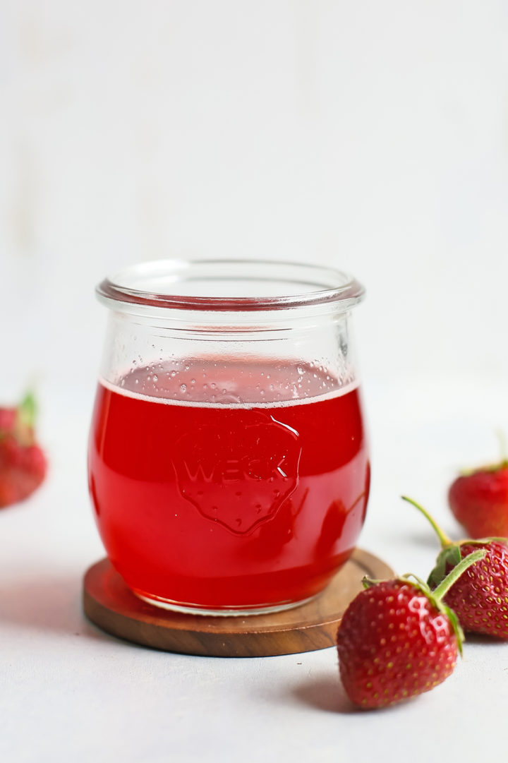 strawberry simple syrup in a glass jar surrounded by fresh strawberries