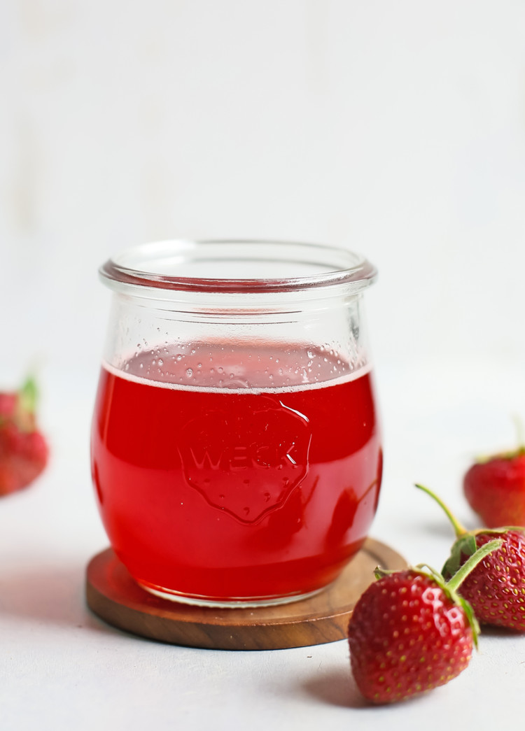 strawberry simple syrup in a glass jar surrounded by fresh strawberries