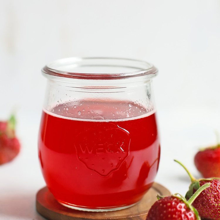 strawberry simple syrup in a glass jar surrounded by fresh strawberries