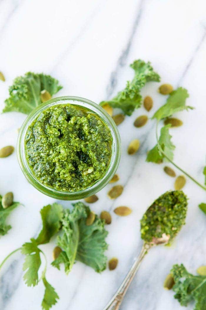 Kale Cilantro Pesto in glass jar with spoon and fresh kale on countertop