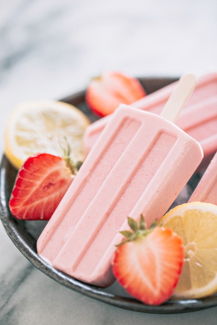 strawberry popsicles in metal bowl with sliced berries and lemons