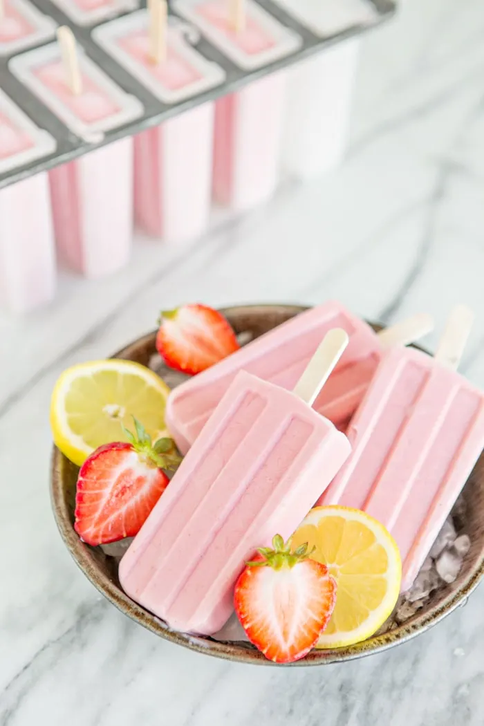 strawberry popsicles in metal bowl with sliced berries and lemons