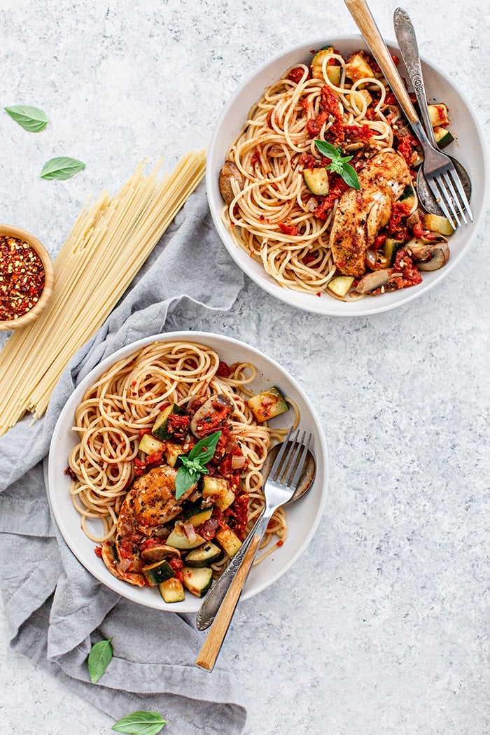 two white bowls of pasta with chicken and tomatoes