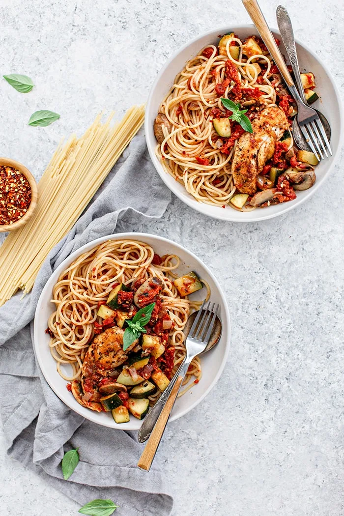 two white bowls of pasta with chicken and tomatoes