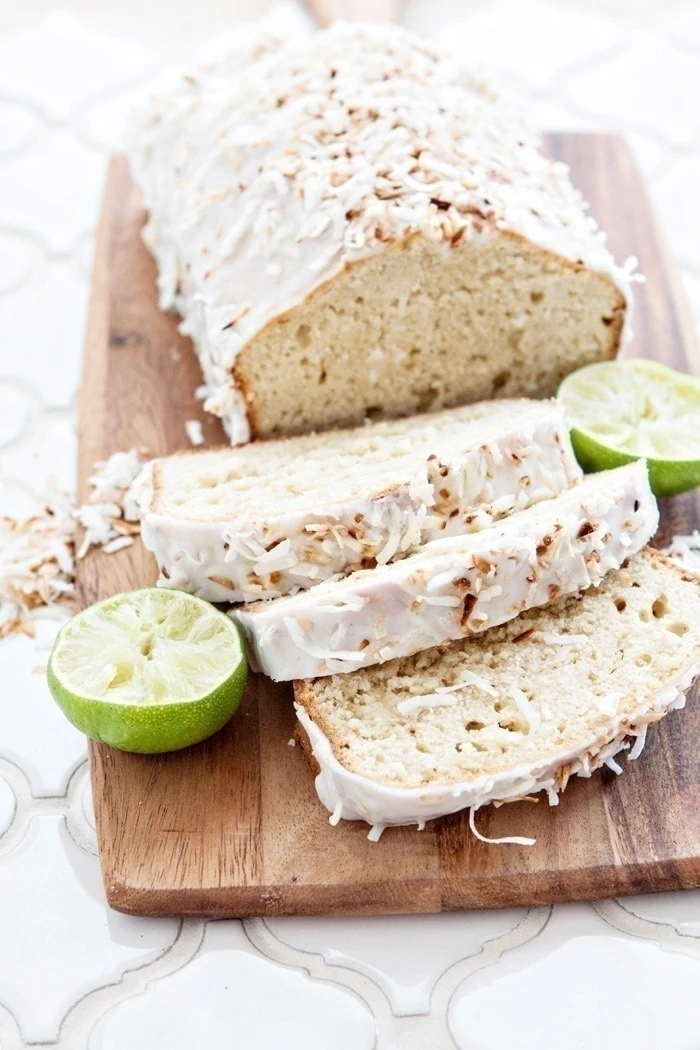 a photo of slices of coconut and banana bread on a cutting board with limes and toasted coconut