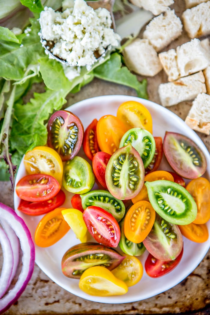 colorful heirloom tomatoes on a white plate next to cubed bread and blue cheese crumbles to use in a blt salad