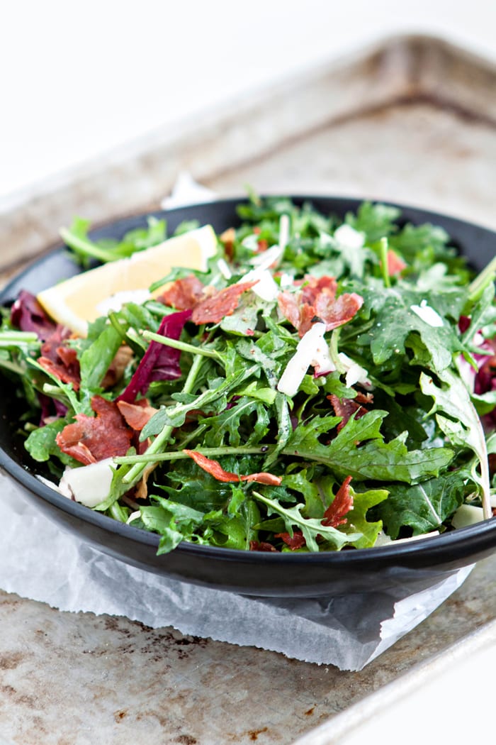 photo of Italian Mixed Greens Salad with Prosciutto and Lemon Dijion Vinaigrette photo in a black bowl for serving with pasta caprese