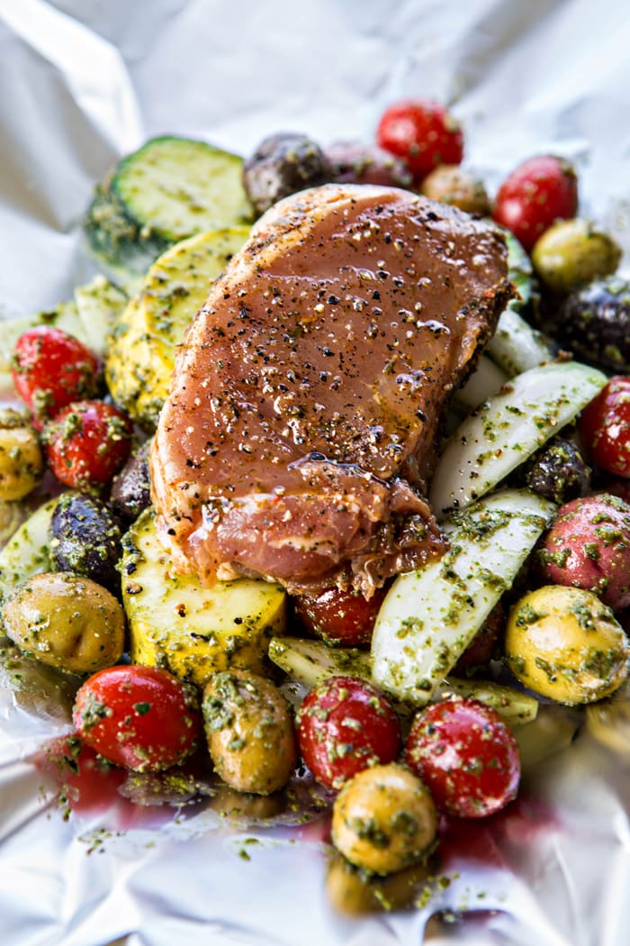 a photo of assembly of foil packet pesto pork chops with summer vegetables