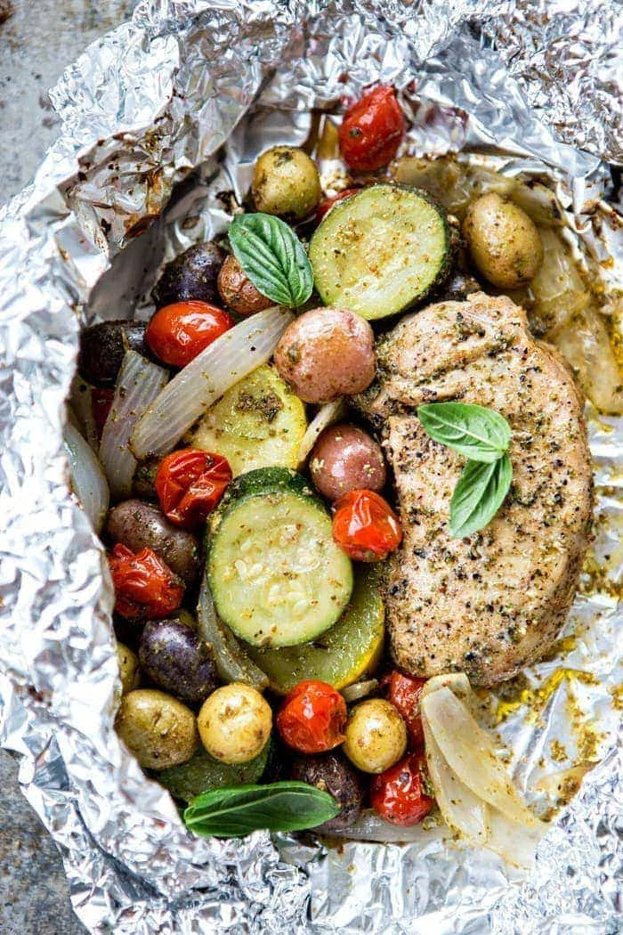 overhead photo of pesto pork chops with summer vegetables cooked in a foil packet