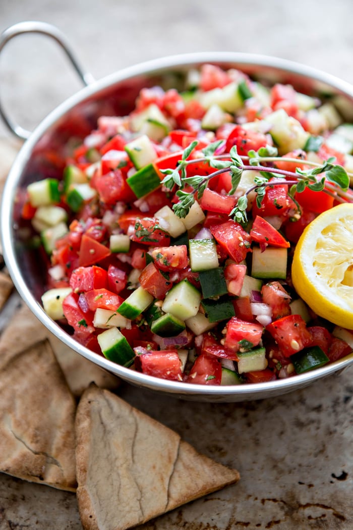photo of a light summer appetizer in a  bowl - cucumber pico de gallo with fresh oregano and a slice of lemon on top