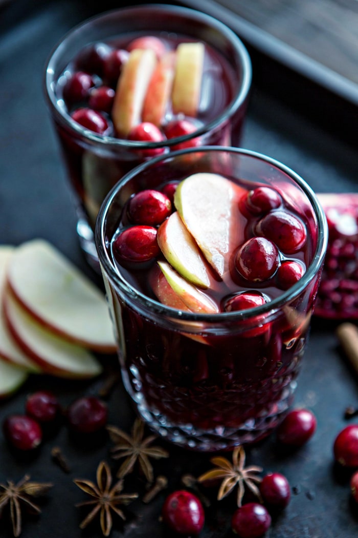 two glasses of hot mulled wine garnished with cranberries and apple slices