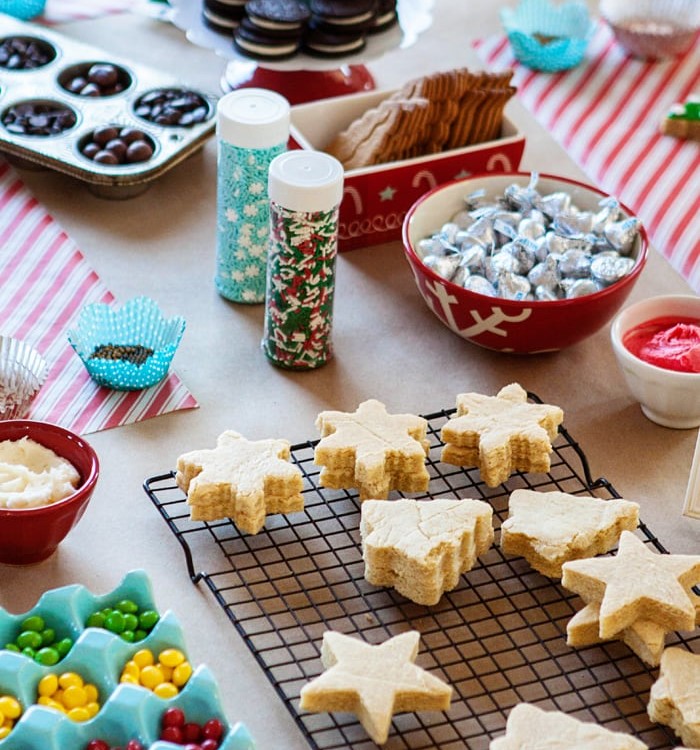 table of christmas cookies and decor items for a kids christmas cookie decorating party