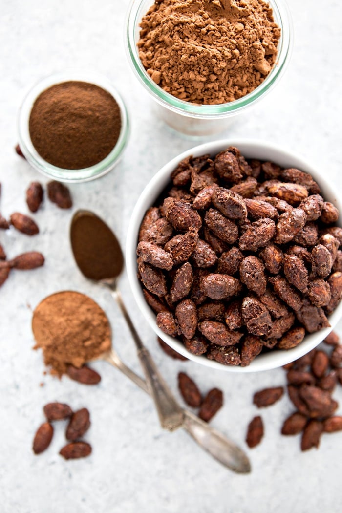 mocha roasted almonds in white bowl next to cocoa powder and espresso powder