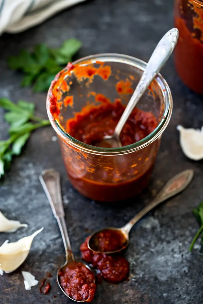 jar of homemade marinara sauce with spoons on counter in front of it