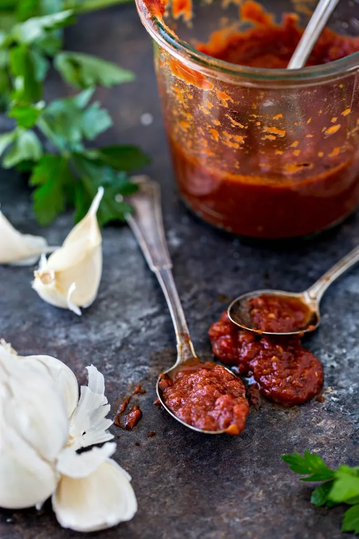 jar of marinara sauce behind two spoons and fresh garlic